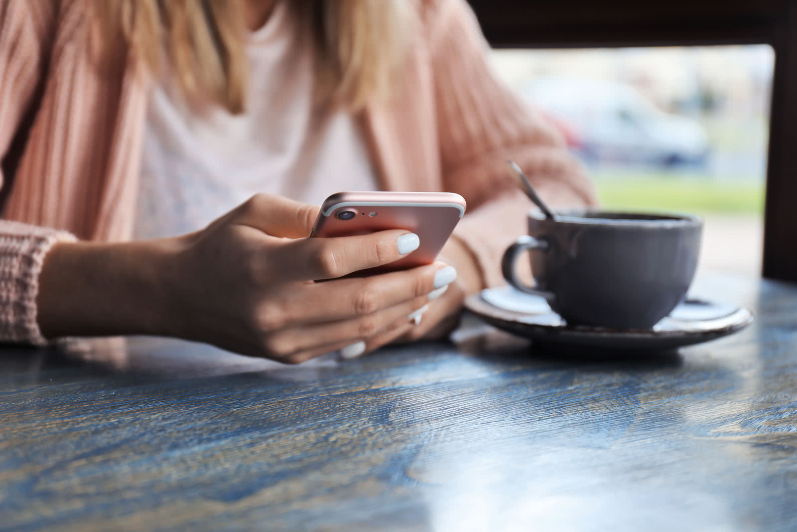 Woman sitting at a table browsing direct lender loans on her pink mobile phone