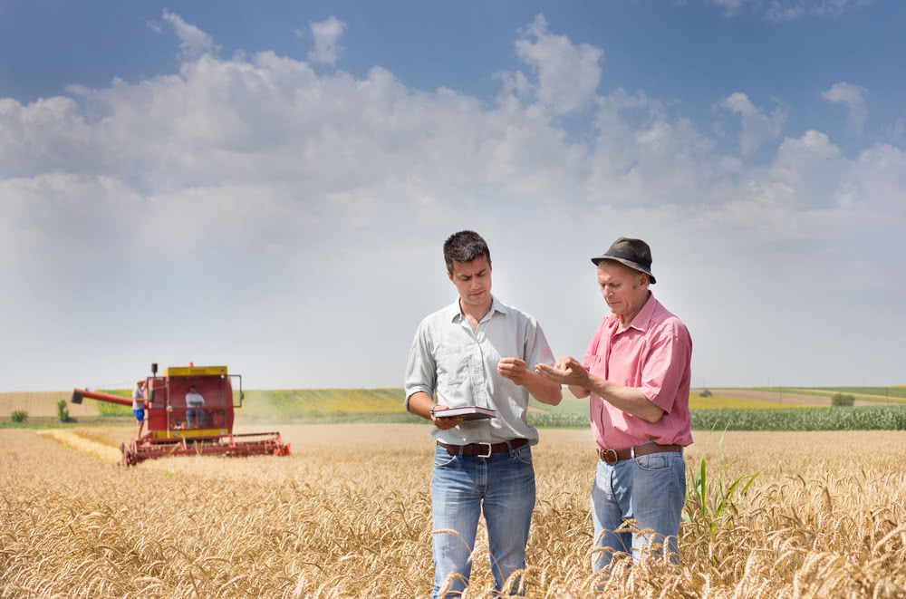 Two farmers in a field discuss offering a new service after a business loss