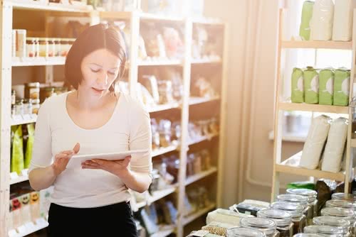 Female owner of local grocery store researching business loans for women with bad credit on tablet 