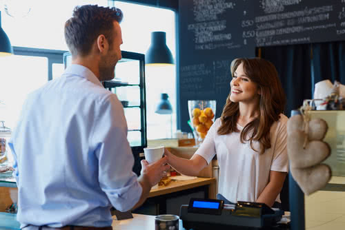 Female coffee shop business owner serves a male customer 