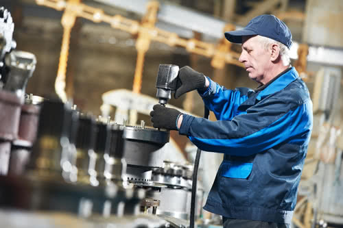 Business owner works on heavy equipment while assembling a manufacturing workshop