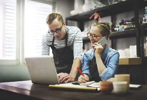 Two craftspeople research CRM platforms on a laptop 