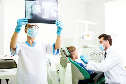 entist is looking at x-ray from new machine. Another dentist treats a patient in the background.