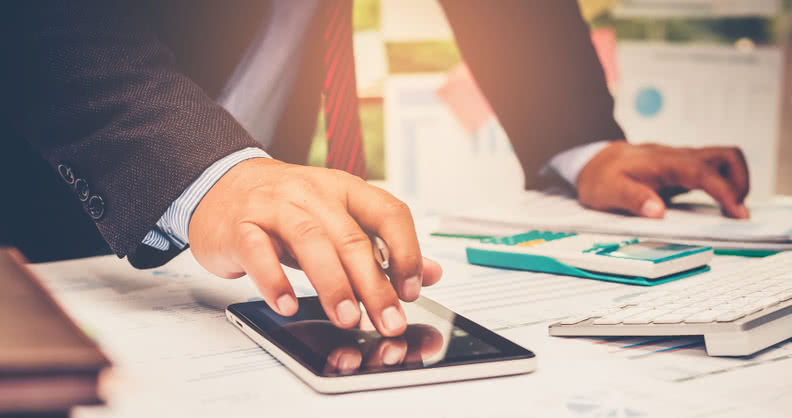 A businessman analyzing investment charts at his workplace and using his tablet ,stock chart , calculator with close up vintage style.